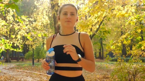 Portrait of Beautiful Smiling Young Woman Running at Park and Drinking Water From Bottle
