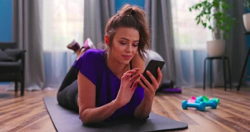 Woman Using Smartphone on Exercise Mat Indoors