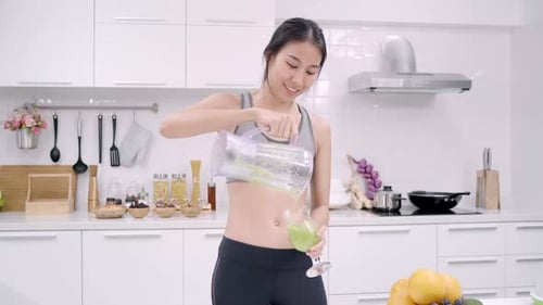 Woman in Kitchen Pours and Drinks Green Smoothie