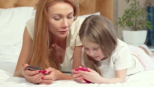 Mother and Daughter Lying on Bed with Phones