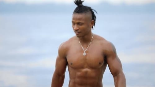 Sexy Macho Man with Muscular Body Comes Out of the Water on Beach Under Rain