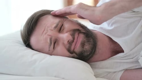 Nahaufnahme eines schlaflosen Bartes junger Mann mit Kopfschmerzen im Bett