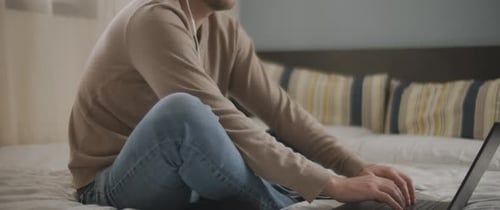 Man Using Laptop On Bed Wearing Headphones