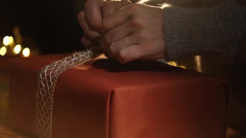 Hands Tying Festive Ribbon on Red Gift Box