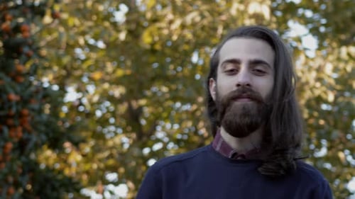 Young long-haired man finds peace in nature. Tangerine trees on the background.