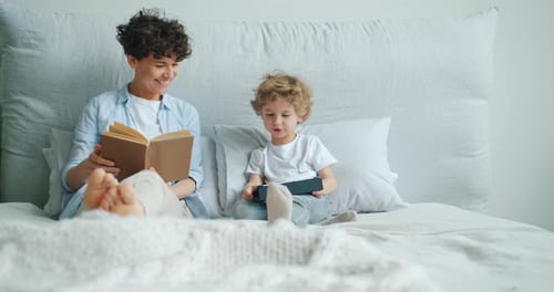 Mother and Child Relaxing on Bed with Book and Tablet