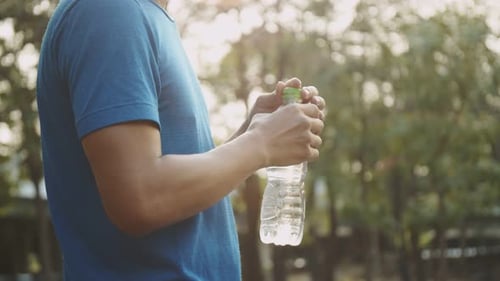 Attractive Asian sportsman runner drinking water while standing taking a break beautiful sunset.