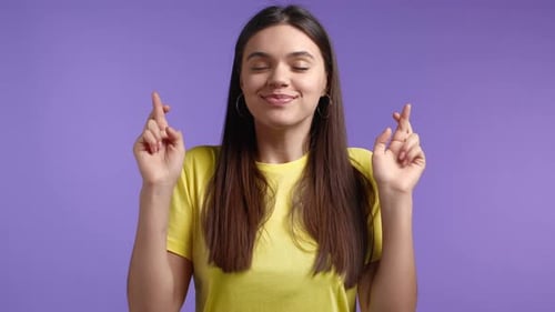 Woman Smiling and Crossing Fingers on Purple Backdrop