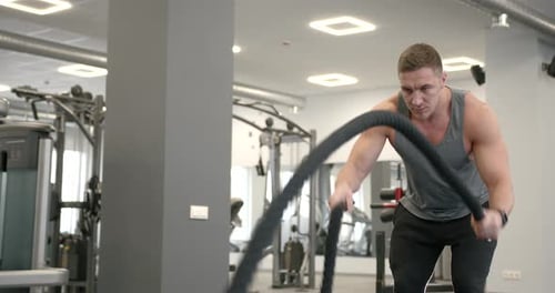 Athletic Guy Focused on Fitness Workout with Ropes in the Gym
