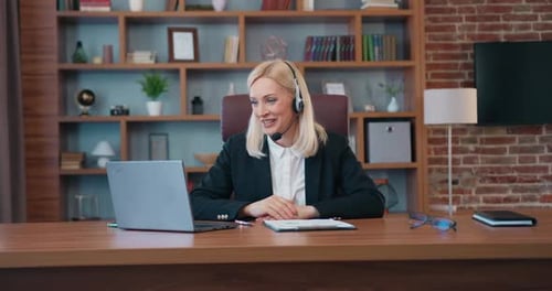 Empresaria con auriculares realizando videoconferencia en un ordenador portátil con sus colegas