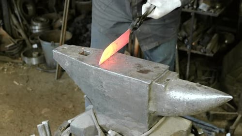 Craftsman Shapes Hot Metal with Hammer and Anvil