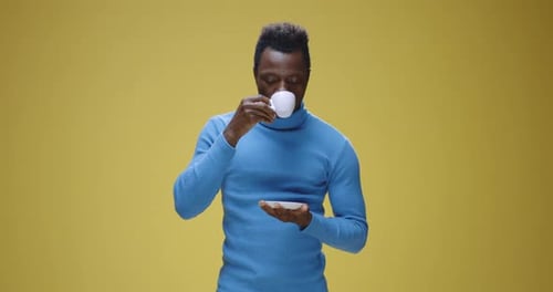 Young Man Drinks Tea and Smiles on Yellow