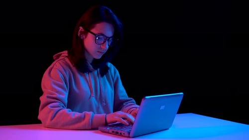 Young Woman with a Laptop. A Woman Is Using a Laptop. Blue and Red Light Falls on a Woman on a Black