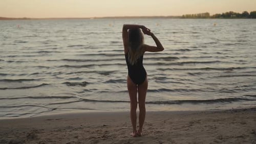 Silhouette Fit and Slim Woman Practices Yoga on a Sandy Beach Against Evening Lake
