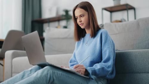 Woman Works on Laptop Taking Notes at Home