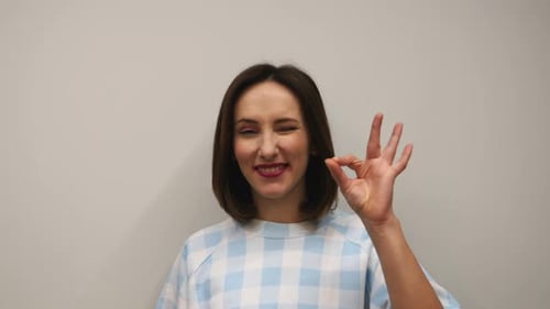 Female doing ok gesture in studio against white wall.