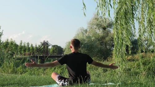 Young Adult Meditating in Park Near River