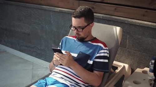 Young Adult Relaxing and Looking at Phone Outside