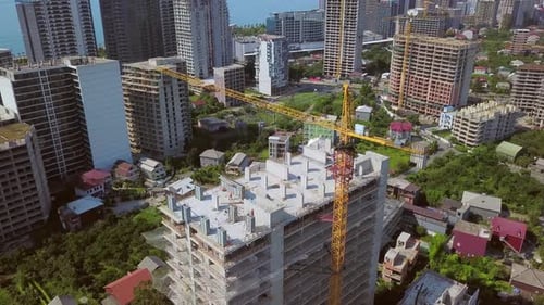 Construction crane on construction site against backdrop of mountains and city.