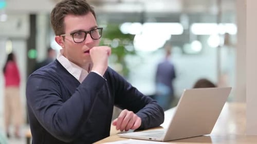 Young Adult Coughing While Using Laptop in Office