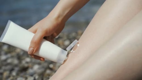 Close Up of Woman Applying Sunscreen To Her Legs on Tropical Beach
