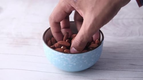 Close Up of Hand Picking Almond From a Bowl