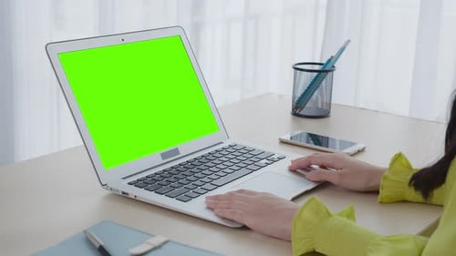 Young asian business woman working on laptop computer with green screen mockup at home.