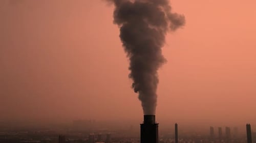 Factory Chimney Emitting Black Smoke Over City at Sunset