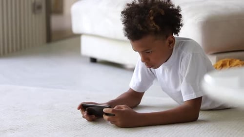 Child Plays Mobile Games Lying on Carpet