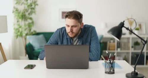 Man Works on Laptop at Desk in Home Office