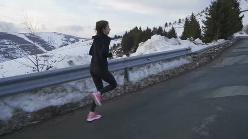 Jogger in Sportswear Training in the Snowy Mountain on Sunset