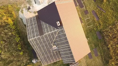 Aerial view of unfinished house with wooden roof structure covered with metal tile sheets under