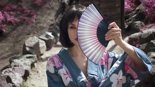 Nahaufnahme einer kaukasischen Geisha-Frau im traditionellen japanischen Kimono bedeckt ihr Gesicht mit Holz