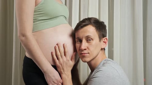 Un homme caresse et écoute un bébé à naître dans le ventre de sa femme