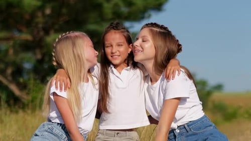 Three Little Girls are Sitting on the Green Grass They are Sincerely Hugging