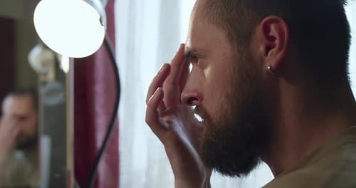 Man Applies Makeup in Front of Mirror