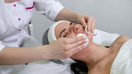 Beautician cleansing face of woman in beauty salon
