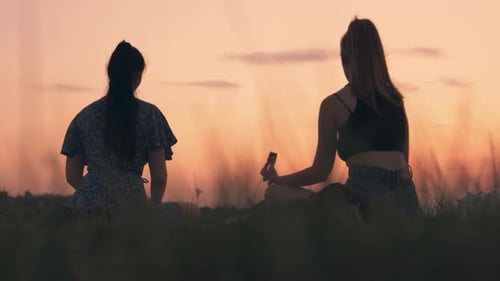 Young Women Meditating in Field at Sunset