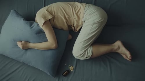 Distressed Young Woman Lying on Couch near Pills
