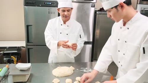 Asian male chefs in uniforms are preparing to bake bread in a stainless kitchen.