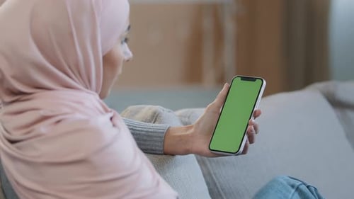 Over Shoulder Business Woman Islamic Arabian Girl in Hijab Sit on Cozy Sofa at Home Hold Mobile in