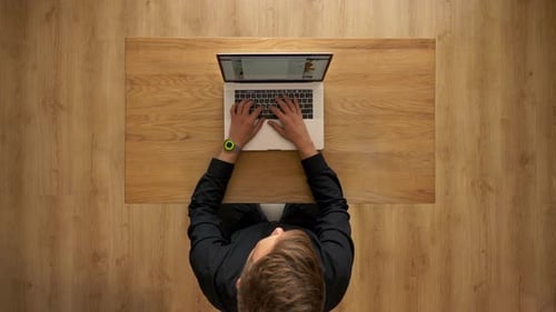 Young Adult Typing on Laptop at Wooden Desk