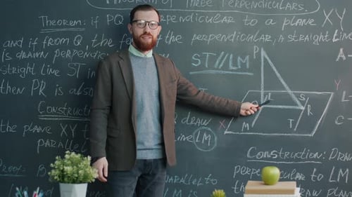 College Professor Giving Maths Lecture Speaking and Pointing at Chalk Board Looking at Camera