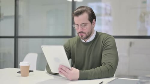 Young Businessman Celebrating Success on Tablet in Office
