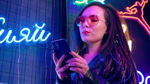 Woman Smiling with Phone Amidst Neon Lights at Night