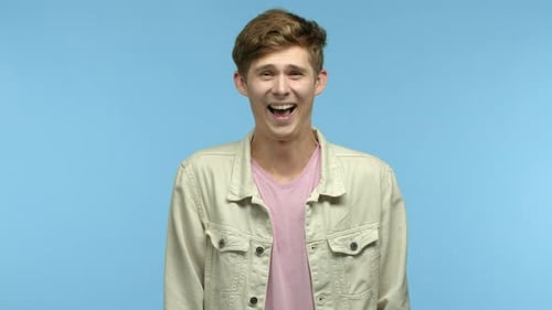 Lustiger junger Mann, der lacht und in die Kamera schaut, wie etwas Lustiges über Joke Standing kichert