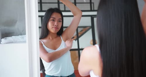 Young Woman Applying Deodorant in Bathroom Mirror