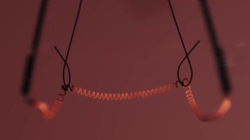The Tungsten Filament in a Glass Lamp Closeup in Slow Motion on Red Background