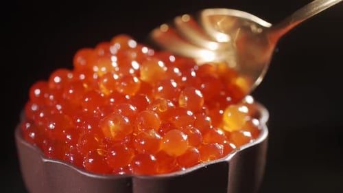 Scoops Red Caviar From a Clay Bowl with a Golden Spoon