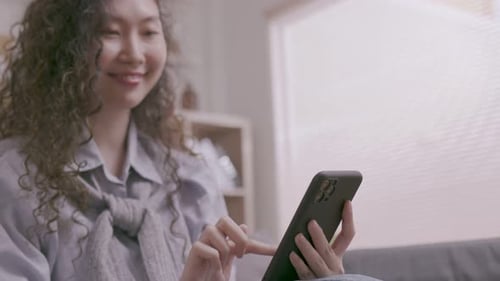 Asian woman Sitting on the sofa in the house, an Asian man works on his tablet.woman works while usi